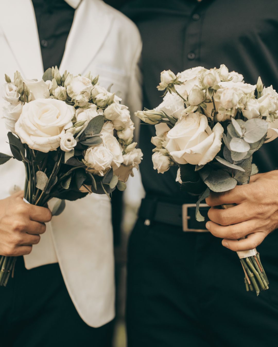 Two grooms holding white rose bouquets on their wedding day